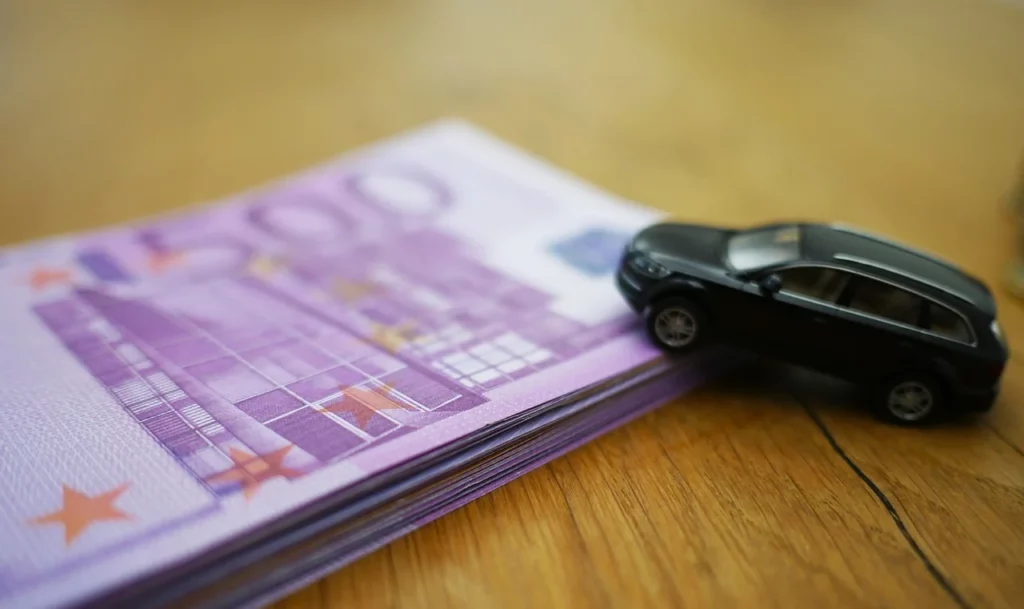 Photo of a toy car placed on a clip of banknotes, representing the import of German cars and their financial impact.